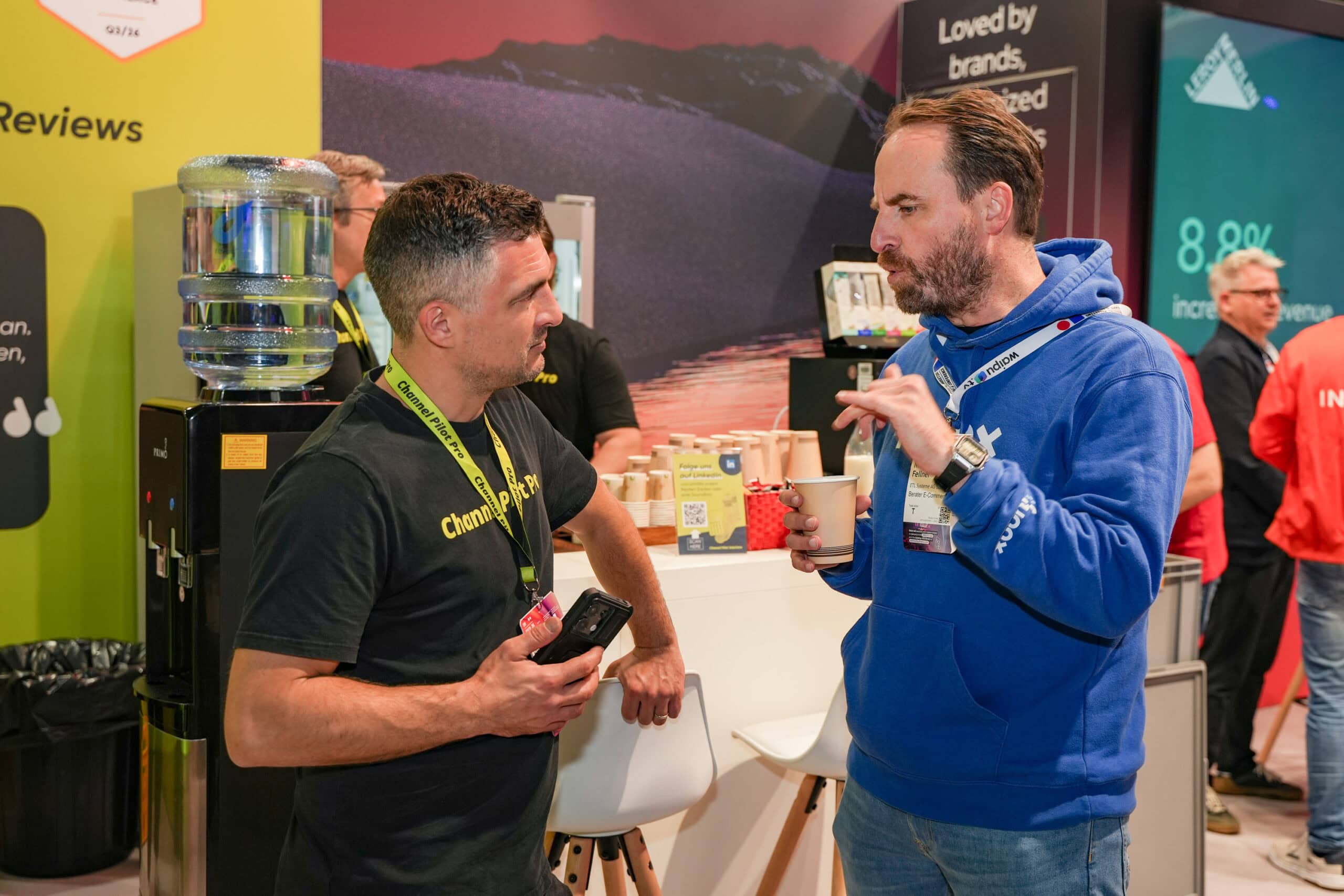 Zwei Männer im Gespräch auf einer Messe, einer hält ein Smartphone.