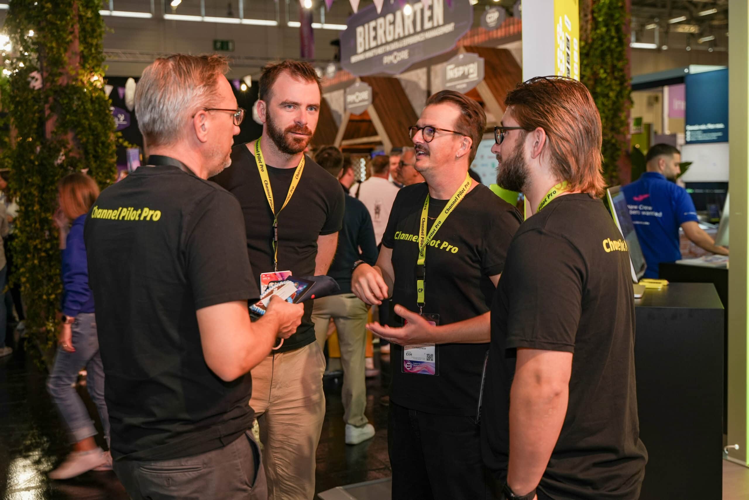 Geschäftsleute im Gespräch auf einer Messe, tragen schwarze T-Shirts mit 'Channel Pilot Pro'.